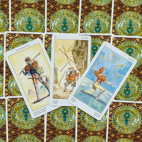 Tarot kortos — trys atverstos lazdų (Wands) kortos akvareliniais piešiniais centre ant turkio‑auksinės nugarėlės, skirtos trijų kortų sklaidai