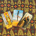 Tarot kortos trijų kortų išklotinė: Monetų karalienė, Lazdų tūzas ir Monetų karalius ant raštuoto fono, pasvirus kampas
