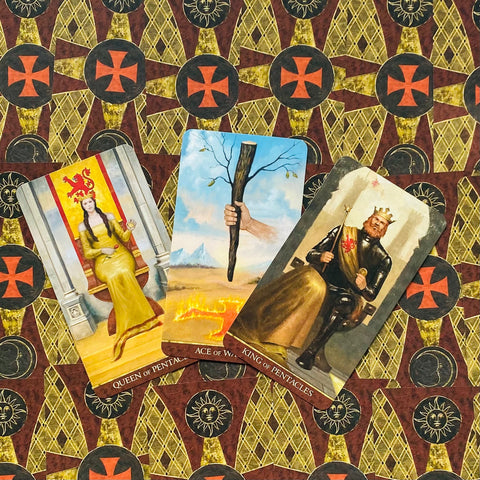 Tarot kortos trijų kortų išklotinė: Monetų karalienė, Lazdų tūzas ir Monetų karalius ant raštuoto fono, pasvirus kampas
