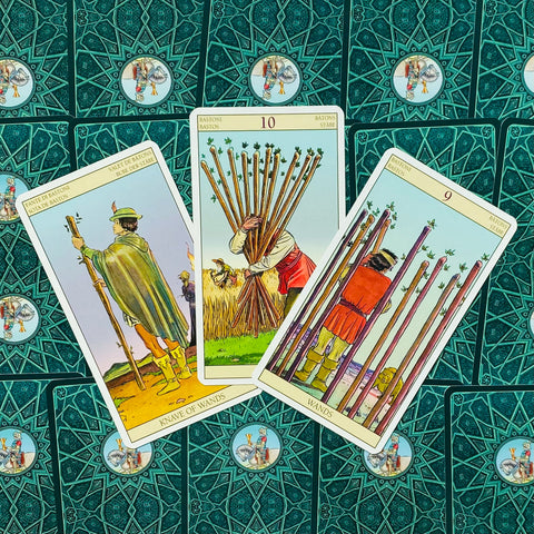 tarot kortos Rider–Waite stiliaus, trys lazdų kortos (Jaunuolis, 10 ir 9) atverstos ant žalsvos ornamentuotos nugarėlės