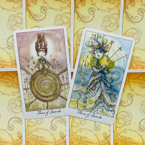 tarot kortos dvi pastelinės kortos (Three of Swords ir Four of Swords) priekinės pusės, švelniai persidengiančios ant geltonų nugarėlių
