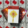 Tarot kortos Notoria: baltas dėklas su auksiniu saulės motyvu, dvi iliustruotos kortos ir raudonas viršelis fone
