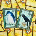 oracle kortos su gyvūnų motyvais — artimas dviejų kortų rinkinys: mėlynas pasakų pingvinas (Willpower) ir juodas varnas (Magick) ant geltono ornamentuoto fono