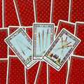 Tarot kortos atverstos trijų kardų kortų fone ant raudonų nugarėlių, akcentas – kardų motyvai ir detalės