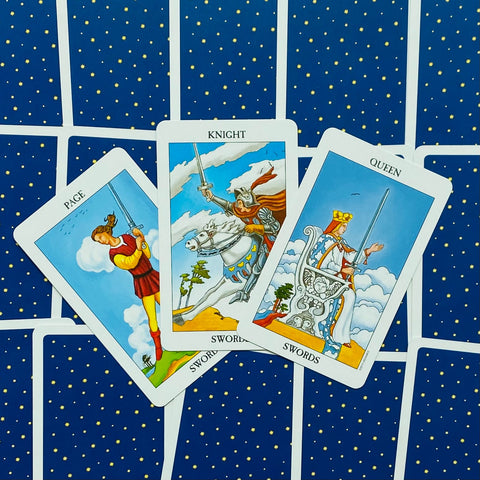 Tarot kortos Rider–Waite Swords komplektas: trys atverstos kortos (Page, Knight, Queen) ant mėlyno žvaigždėto nugarėlio