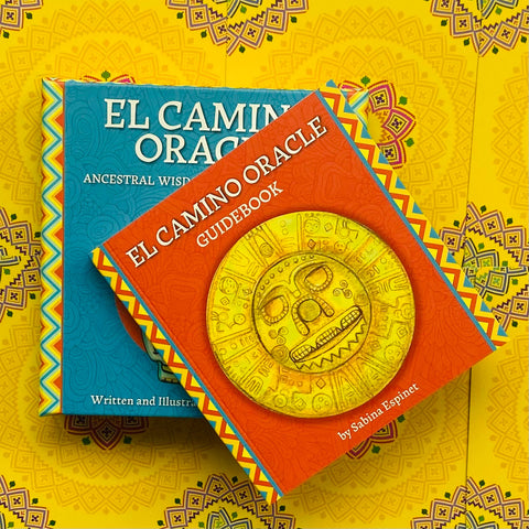 El Camino Oracle kortų rinkinys su ryškiu raudonu guidebook ir mėlyna dėže, viršuje persidengiantys viršeliai su auksiniu disku