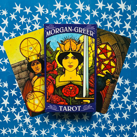 Tarot kortos Morgan‑Greer su spalvotu dėklu ir trimis išskleistomis kortomis ant mėlyno fono su baltomis žvaigždėmis