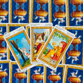 Tarot kortos su kačių iliustracijomis, trys atverstos kortos su aukso rėmais centre ant mėlyno ornamentuoto galinio rašto