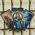 Tarot kortos CatTarot — dėžutė priekyje ir trys atverstos kortos su katėmis, ryškūs mėlyni ir auksiniai motyvai