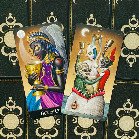 Tarot kortos, dvi kupų kortos (Ace ir Three of Cups) parodytos iš priekinio plano ant juodo ornamentuoto dėklo