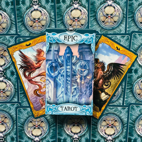 Tarot kortos Epic dėžutėje su mėlynais ornamentais ir auksiniais rėmeliais bei dviem iliustruotomis kortomis šonuose