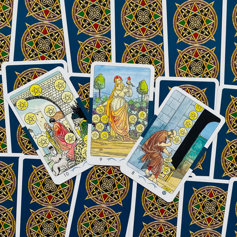 Tarot kortos Rider‑Waite: trys atverstos pentaklių kortos (8, 9, 10) ant mėlyno ornamentuoto nugarėlių fono