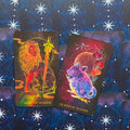 tarot kortos King of Wands ir Queen of Wands — spalvingos kosminės iliustracijos priekyje ir mėlynos žvaigždėtos nugarėlės