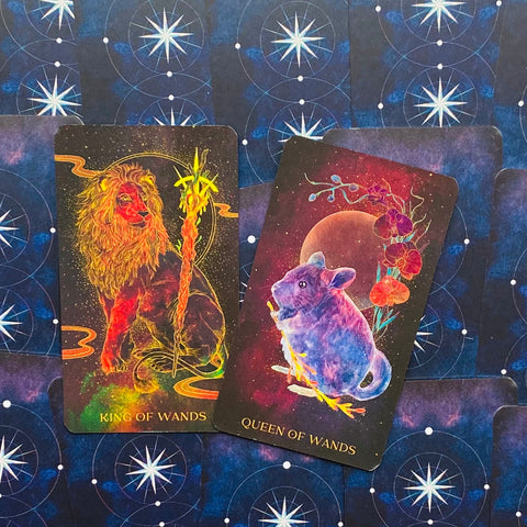 tarot kortos King of Wands ir Queen of Wands — spalvingos kosminės iliustracijos priekyje ir mėlynos žvaigždėtos nugarėlės