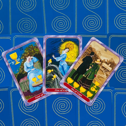 Tarot kortos su taurėmis (4, 5, 6) fanuotos kampu, ryškūs violetiniai rėmeliai ir mėlyni spiralės nugarėlės