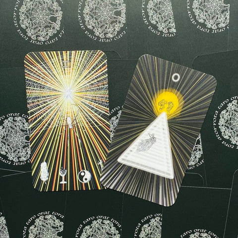 tarot kortos Orat Tora — dvi atvertos juodos kortos su geltonai auksiniais spinduliais, smulkiais simboliais ir trikampio motyvu
