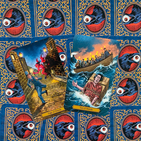 Tarot kortos, dvi atverstos – Page of Wands ir Ten of Wands su dramatiniais scenomis ant mėlyno snapo rašto