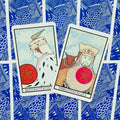 Tarot kortos Queen ir King of Pentacles kampu išdėstytos ant mėlynos raštuotos nugarėlės, matomas kortų dizainas ir spalvų derinys