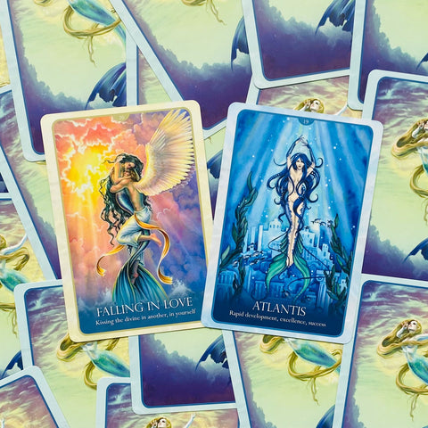Tarot kortos su orakulo iliustracijomis, dvi atverstos kortos — „Falling in Love“ saulėta rožine palete ir „Atlantis“ mėlyname jūros fone, parodytos iš viršaus