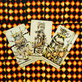 Tarot kortos su oranžinėmis rombų nugarėlėmis — trys atvertos karališkos kortos (Karalius, Karalienė, Riteris) fanuotos, rodant piešinių ir spalvų detales