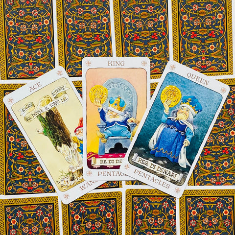 tarot kortos Pentacles komplektas su ornamentinėmis tamsiai geltonomis nugarėlėmis, trys atverstos kortos (karalius, karalienė, tūzas) fanuotai išdėstytos viršuje