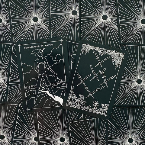Tarot kortos juodos su baltu piešiniu, iš viršaus matomas vienos kortos Philosopher of Knives ir šešių peilių korta