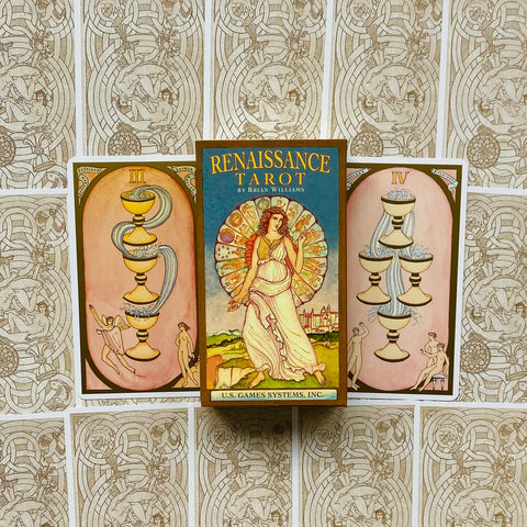 Renaissance Tarot dėžutė priekyje, U.S. Games Systems leidimas ant stalviršio, fone atverstos taurės kortos