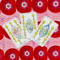 Tarot kortos – trys atverstos Puodelių kortos (7, 8, 9) išdėstytos ant raudono ornamentinio fono, akcentuoja kortų simboliką