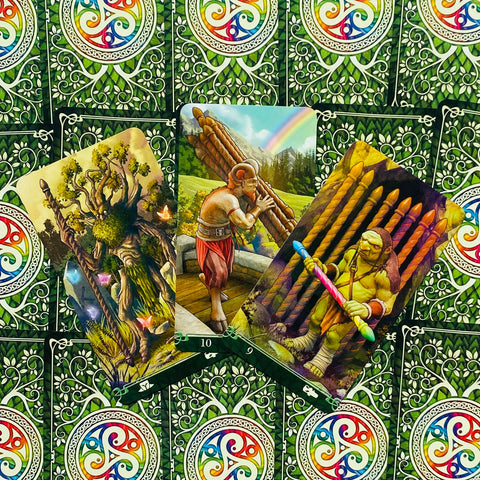 Tarot kortos su žaliais nugarėliais, centre trys atverstos spalvingos kortos: medžio, nešulio ir kario motyvai