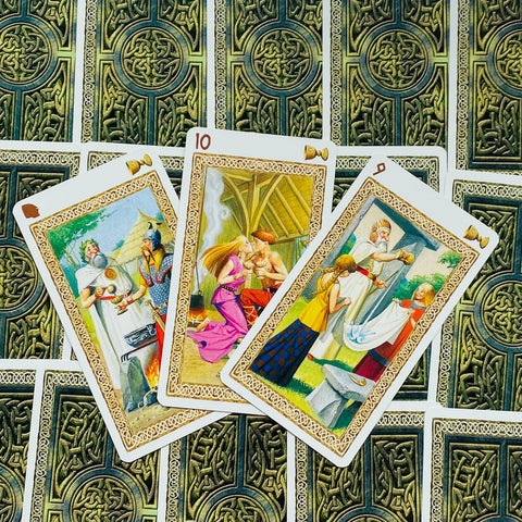 Tarot kortos su keltų nugarėlėmis, trys atvertos iliustruotos kortos fane, artimas planas akcentuoja auksinį rėmelį ir ryškias spalvas