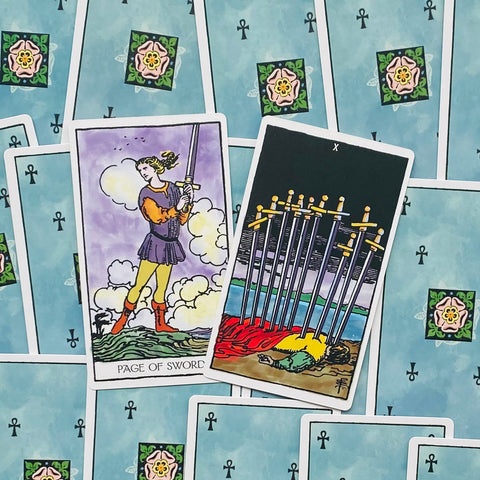 Tarot kortos Rider–Waite stiliaus su melsvomis nugarėlėmis, dvi atverstos kortos – Kardų puslapis ir Dešimt kardų, fotografuota iš viršaus