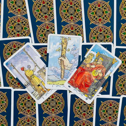 Tarot kortos Rider–Waite stiliaus rinkinys, trys atvertos kortos (Lazda, Dvi Lazdos, Pentaklis) ant mėlynos nugarėlės rašto