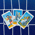 tarot kortos Rider–Waite stiliaus rinkinys, trys taurės kortos (Page, Knight, Queen) ant mėlyno žvaigždėto fono, kampinis išdėstymas