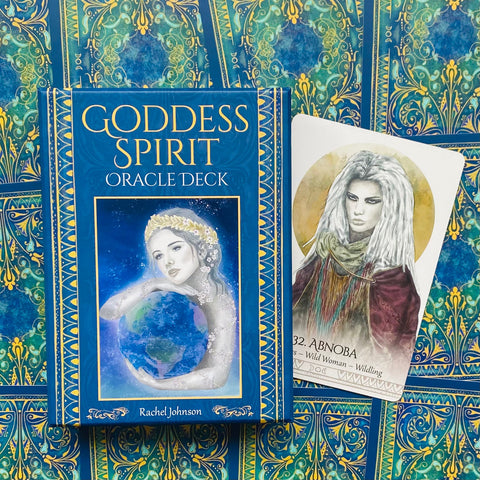 Goddess Spirit orakulo kortos mėlynas dėklas su auksiniu dekoru ir šalia viena atversta korta (Abnoba) ant ornamentuoto fono