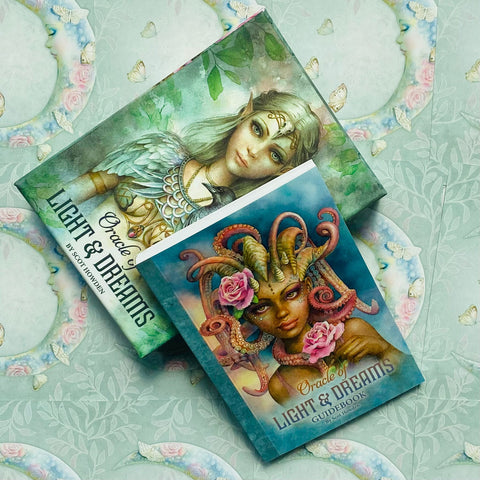 Oracle kortų rinkinys „Light & Dreams“ su gidobuku, plokščias išdėstymas — gidobuko priekinis viršelis su aštuonkojo šukuosena ir viršuje matoma antra dėžutė su elfės portretu