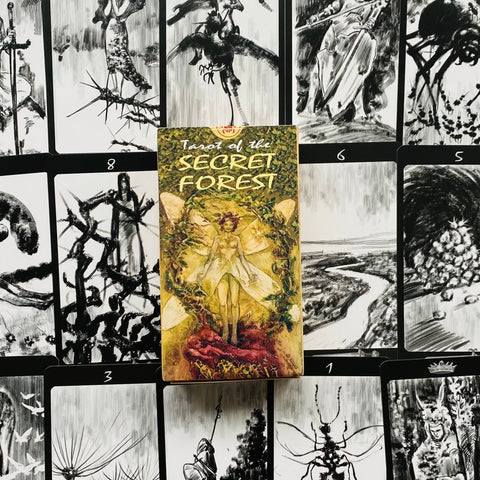 tarot kortos Secret Forest — geltonai žalsva dėžutė stovinti ant juodai baltų iliustruotų kortų, akcentuoja viršelio meną