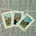 Tarot kortos Rider‑Waite stiliaus, kremiškomis kraštinėmis, trijų taurų kortų išklotinė ant rašto nugarėlių, arti fotografuota
