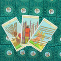 Tarot kortos trys Lazdų kortos (8, 9, 10) išrikiuotos fanu ant žalsvos ornamentuotos kortų nugarėlės, rodantis šio varianto dizainą