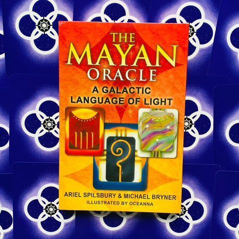 Mayan Oracle kortų rinkinys su ryškiai oranžine dėže ir trimis pavyzdiniais kortų simboliais, padėtas ant mėlyno raštuoto fono