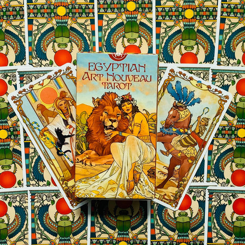 Taro kortų rinkinys Egyptian Art Nouveau Tarot — dėžutė ir trys atverstos kortos su art nouveau Egipto motyvais, fone skarabėjų raštas