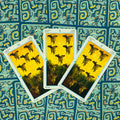 Tarot kortos — trys atvertos taurų kortos (8, 9, 10) su geltonu piešiniu ant mėlyno raštuoto nugarėlių fono
