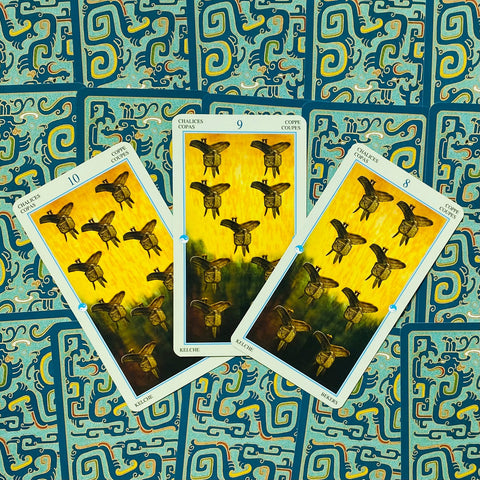 Tarot kortos — trys atvertos taurų kortos (8, 9, 10) su geltonu piešiniu ant mėlyno raštuoto nugarėlių fono