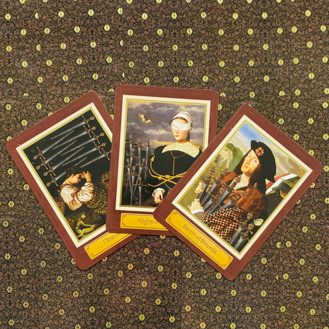 Tarot kortos ant raštuoto tamsaus audinio, trys kardų serijos kortos (7, 8, 9) išdėstytos fanu