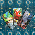 Tarot kortos komplektas: trys atverstos kortos (Karalius ir Karalienė Pentaklių, Lazdų tūzas) ant tamsiai mėlyno žvaigždėto fono, plokščias išdėstymas