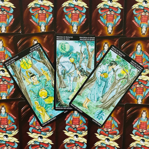 Tarot kortos Pentaklių rūšies – trys akvarelinės kortos (karalius, princesė, princas) žaliai‑mėlynos, išdėstytos ant samurajaus nugarėlių su jin‑jan simboliu