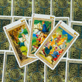 tarot kortos su celtų raštais, trys atvertos kortos centre su spalvingomis liaudies scenomis ir ugnies šokiu