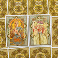 Tarot kortos su Art Nouveau iliustracijomis — dvi atverstos kortos (Vėžys ir Dvyniai) su auksinėmis ornamentuotomis nugarėlėmis