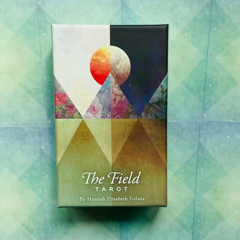 The Field Tarot kortų rinkinys dėžutėje, frontinis vaizdas su geometriniais trikampiais, saulės/menės simboliu ir žaliu‑melsvu fonu