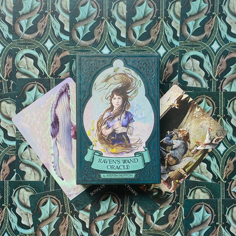 Raven's Wand Oracle kortų rinkinys – tamsiai žalsvame ornate dėkle su moters iliustracija, centrinis, trys išskleistos kortos fone
