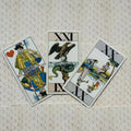 Tarot kortos trijų kortų išdėstymas: centrinė XXI su ereliu, kairė – riteris, dešinė – atversta scena ant raštuoto fono